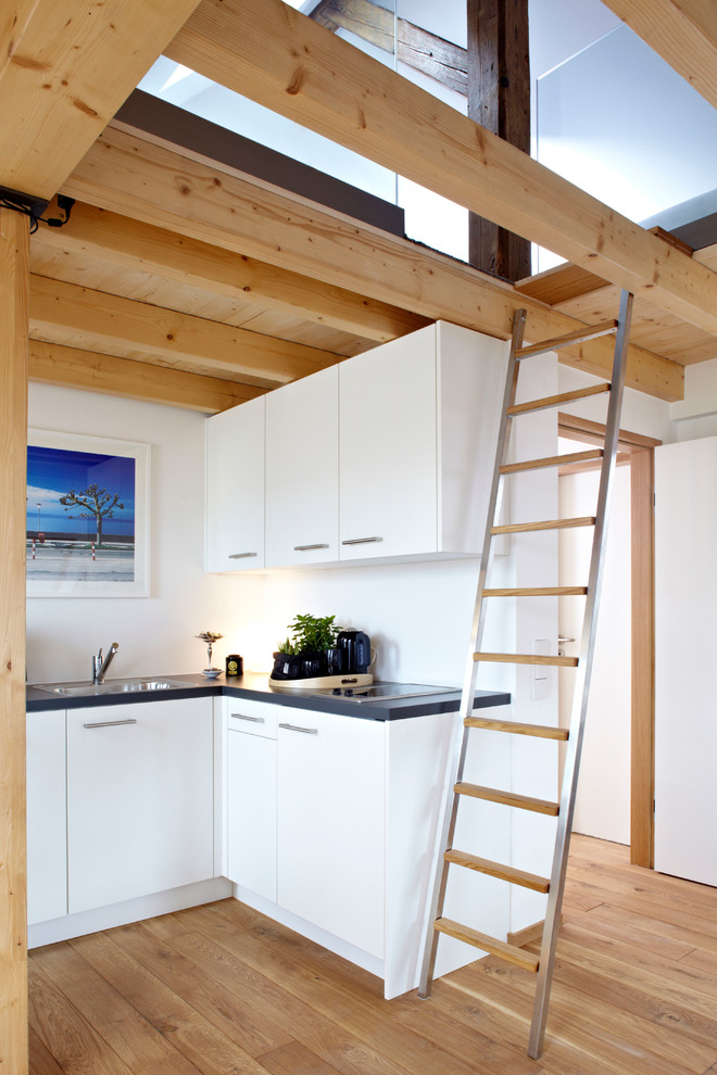Foto på ett litet funkis kök, med en nedsänkt diskho, släta luckor, vita skåp, integrerade vitvaror och mellanmörkt trägolv