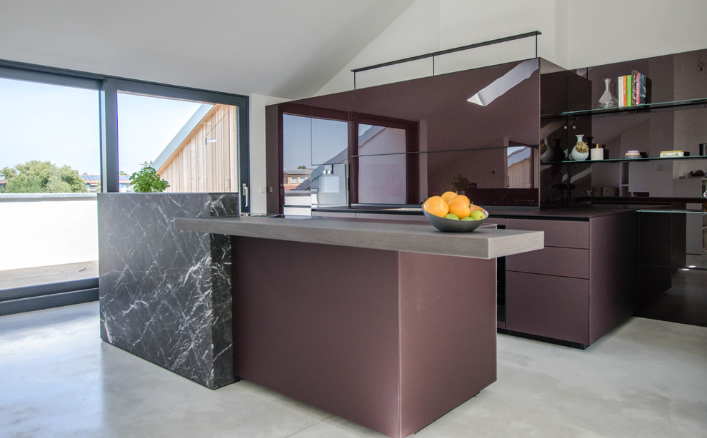 This is an example of an expansive contemporary galley kitchen/diner in Berlin with a single-bowl sink, glass-front cabinets, purple cabinets, glass worktops, glass sheet splashback, black appliances, concrete flooring, an island, grey floors and purple worktops.