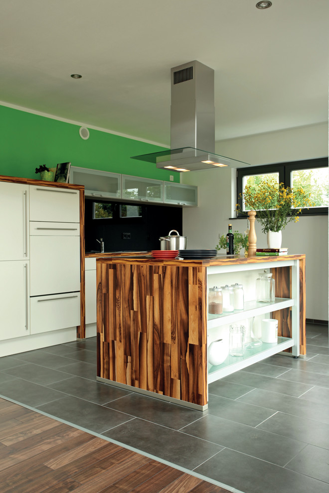 Modern inredning av ett brun brunt kök, med vita skåp, träbänkskiva, svart stänkskydd, rostfria vitvaror, mörkt trägolv, en köksö och brunt golv