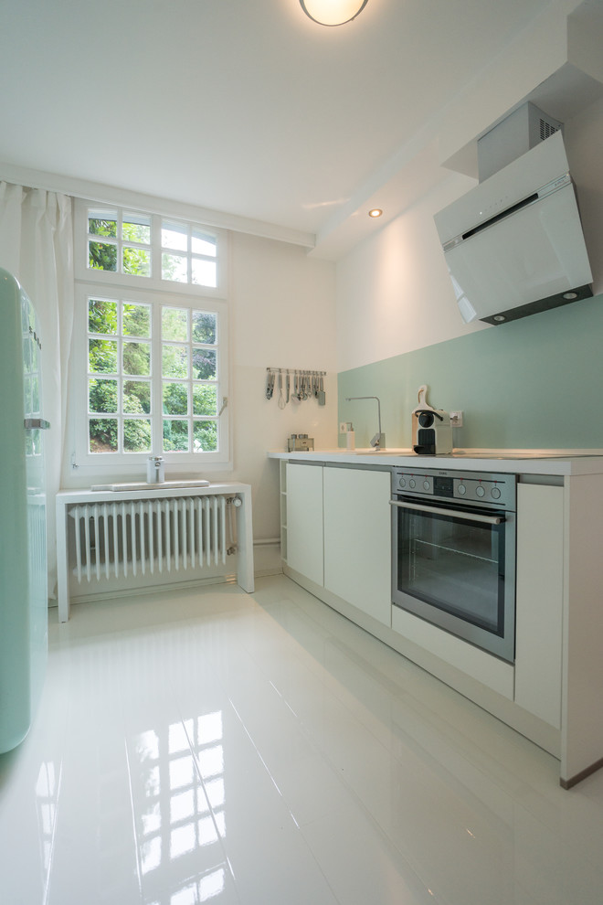 Foto de cocina lineal contemporánea de tamaño medio cerrada sin isla con armarios con paneles lisos, puertas de armario blancas, salpicadero gris y electrodomésticos de acero inoxidable