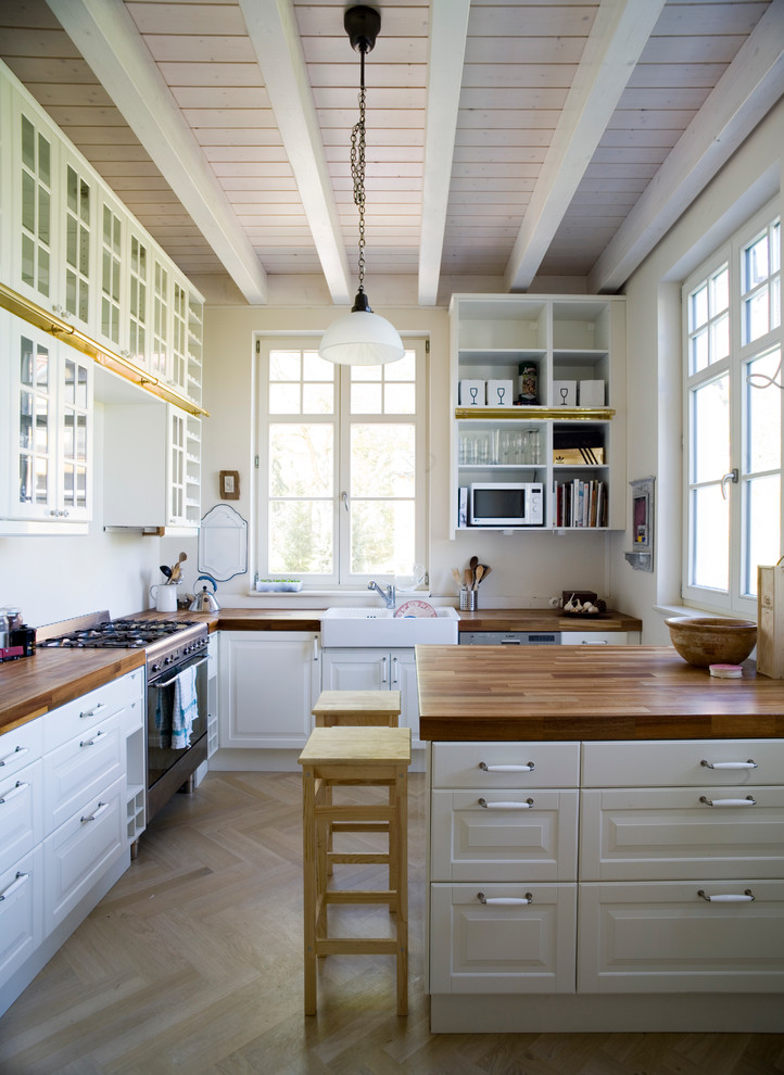 Mid-sized farmhouse l-shaped light wood floor kitchen photo in Berlin with a drop-in sink, beaded inset cabinets, white cabinets, wood countertops, white backsplash, stainless steel appliances and a peninsula