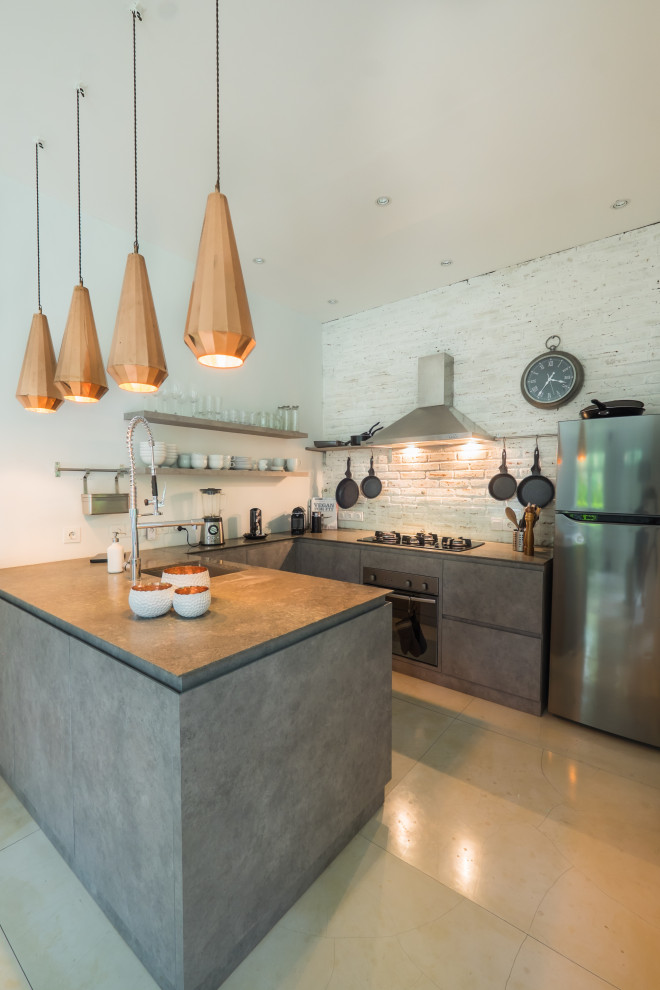 This is an example of a small mediterranean grey and white u-shaped open plan kitchen with a built-in sink, flat-panel cabinets, grey cabinets, marble worktops, white splashback, brick splashback, stainless steel appliances, concrete flooring, an island, beige floors and grey worktops.