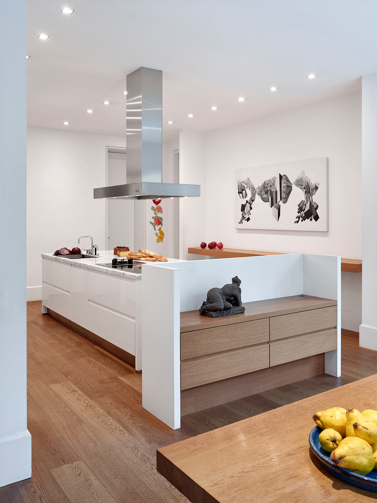 Expansive contemporary galley kitchen/diner in Frankfurt with a built-in sink, flat-panel cabinets, white cabinets, marble worktops, white splashback, medium hardwood flooring, an island, brown floors and white worktops.