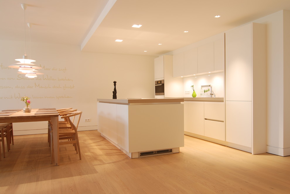 Design ideas for a large contemporary galley kitchen/diner in Hamburg with flat-panel cabinets, white cabinets, white splashback, light hardwood flooring and an island.