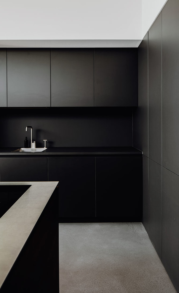 Foto på ett mycket stort funkis svart kök, med en nedsänkt diskho, släta luckor, svarta skåp, svart stänkskydd, svarta vitvaror, betonggolv, en köksö och grått golv