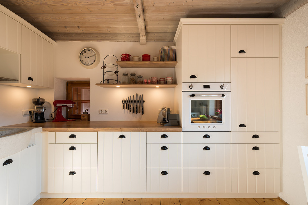 Foto på ett litet lantligt brun kök och matrum, med en rustik diskho, luckor med lamellpanel, vita skåp, träbänkskiva, vita vitvaror, mellanmörkt trägolv, en halv köksö och brunt golv