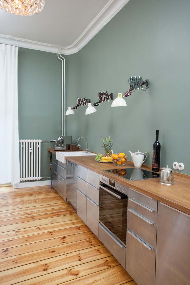 ベルリンにある中くらいなコンテンポラリースタイルのおしゃれなキッチン (エプロンフロントシンク、フラットパネル扉のキャビネット、ステンレスキャビネット、木材カウンター、シルバーの調理設備、淡色無垢フローリング、アイランドなし、ベージュの床、ベージュのキッチンカウンター、緑のキッチンパネル) の写真