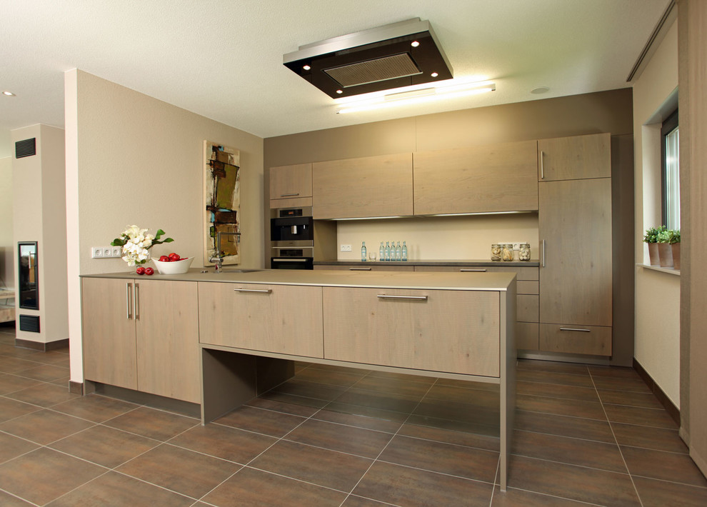 Exemple d'une cuisine ouverte parallèle tendance avec des portes de placard marrons, une crédence beige, un électroménager en acier inoxydable, tomettes au sol, un sol marron et un plan de travail gris.