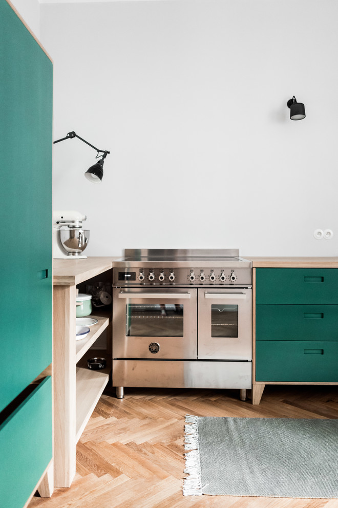 Inredning av ett minimalistiskt mellanstort l-kök, med släta luckor, gröna skåp, träbänkskiva, integrerade vitvaror och ljust trägolv