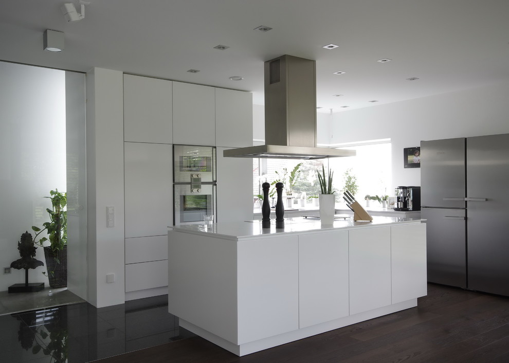 Modern inredning av ett avskilt, mellanstort vit vitt l-kök, med släta luckor, vita skåp, rostfria vitvaror, mörkt trägolv, en köksö och brunt golv