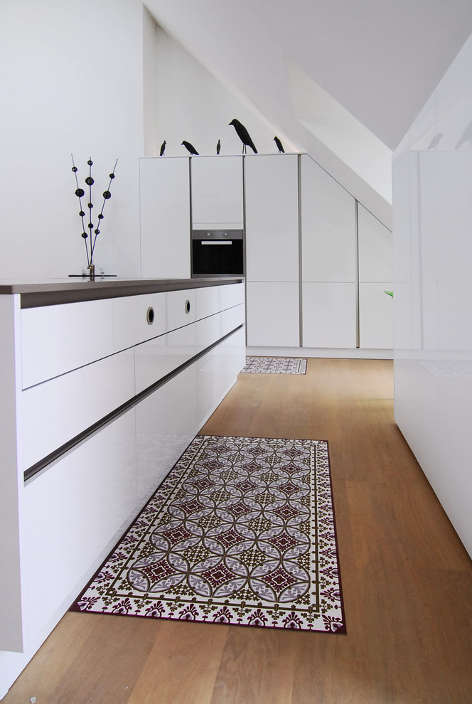 Offene, Zweizeilige, Mittelgroße Moderne grifflose Küche mit flächenbündigen Schrankfronten, braunem Holzboden, schwarzen Elektrogeräten, weißen Schränken und Kücheninsel in München