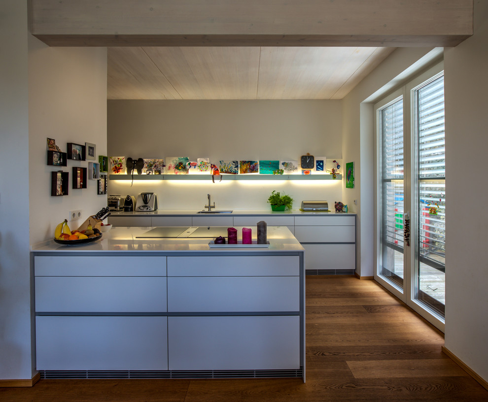 Offene, Einzeilige, Mittelgroße Moderne Küche mit weißen Schränken, Kücheninsel, integriertem Waschbecken, Küchenrückwand in Weiß, gebeiztem Holzboden und braunem Boden in Köln