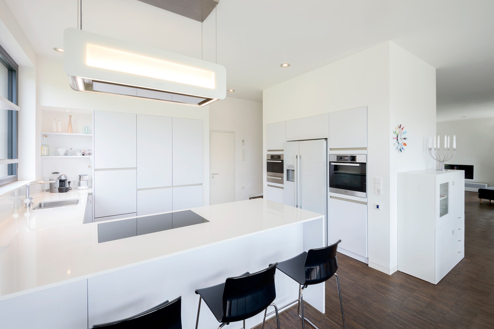 ニュルンベルクにある広いコンテンポラリースタイルのおしゃれなキッチン (ドロップインシンク、フラットパネル扉のキャビネット、白いキャビネット、白いキッチンパネル、ガラス板のキッチンパネル、パネルと同色の調理設備、濃色無垢フローリング) の写真