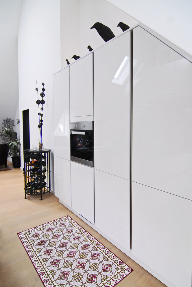 Ispirazione per una piccola cucina minimal con ante lisce, ante bianche, pavimento in legno massello medio e elettrodomestici neri