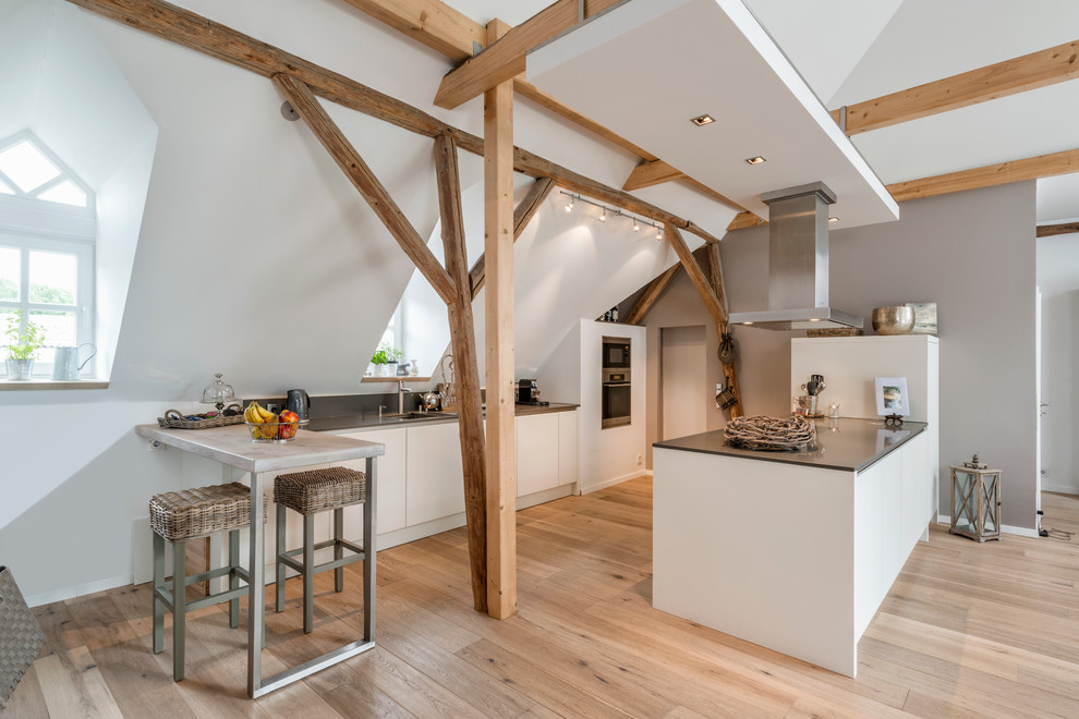 Foto på ett stort nordiskt kök med öppen planlösning, med en köksö, vita skåp, ljust trägolv, släta luckor, en enkel diskho och rostfria vitvaror