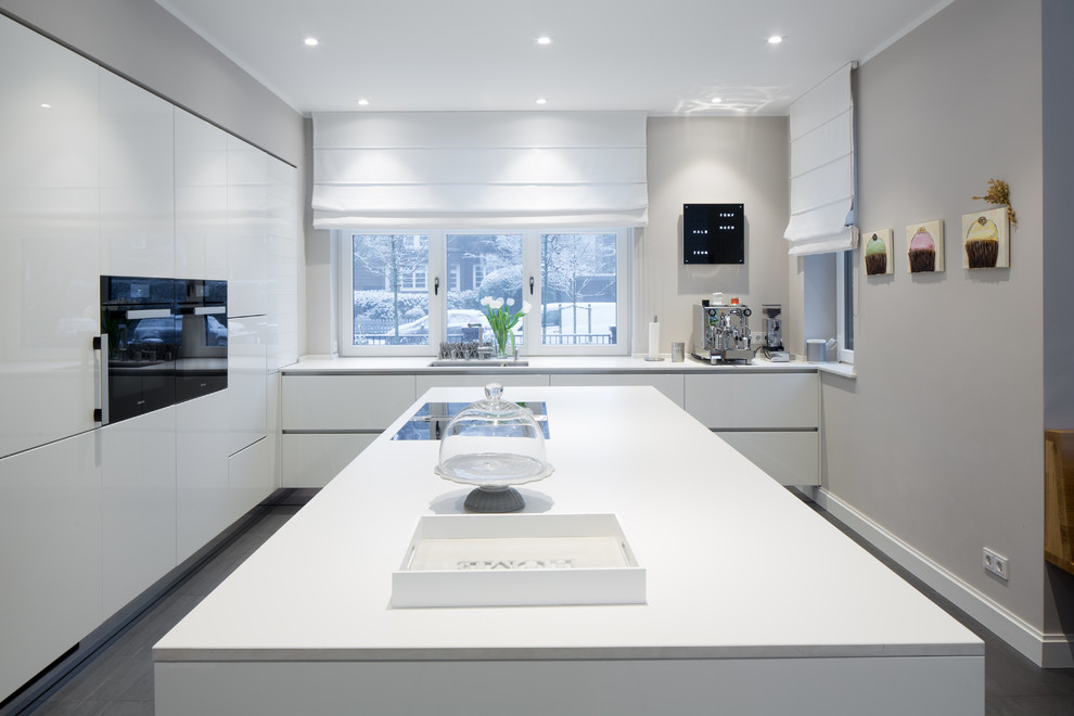 Geschlossene, Mittelgroße Nordische Küche in L-Form mit integriertem Waschbecken, flächenbündigen Schrankfronten, weißen Schränken, Küchenrückwand in Weiß, schwarzen Elektrogeräten, Kücheninsel und grauem Boden in Hamburg
