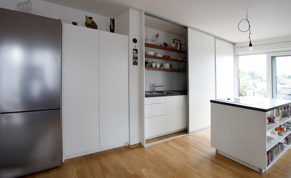 Design ideas for a medium sized contemporary single-wall open plan kitchen in Nuremberg with a submerged sink, flat-panel cabinets, white cabinets, light hardwood flooring, an island and beige floors.