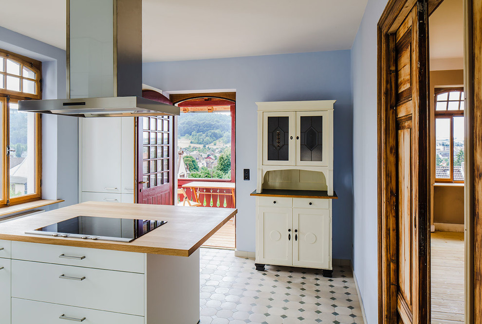 Geschlossene Landhaus Küche mit Schrankfronten im Shaker-Stil, weißen Schränken, Arbeitsplatte aus Holz, Kücheninsel und buntem Boden in Frankfurt am Main