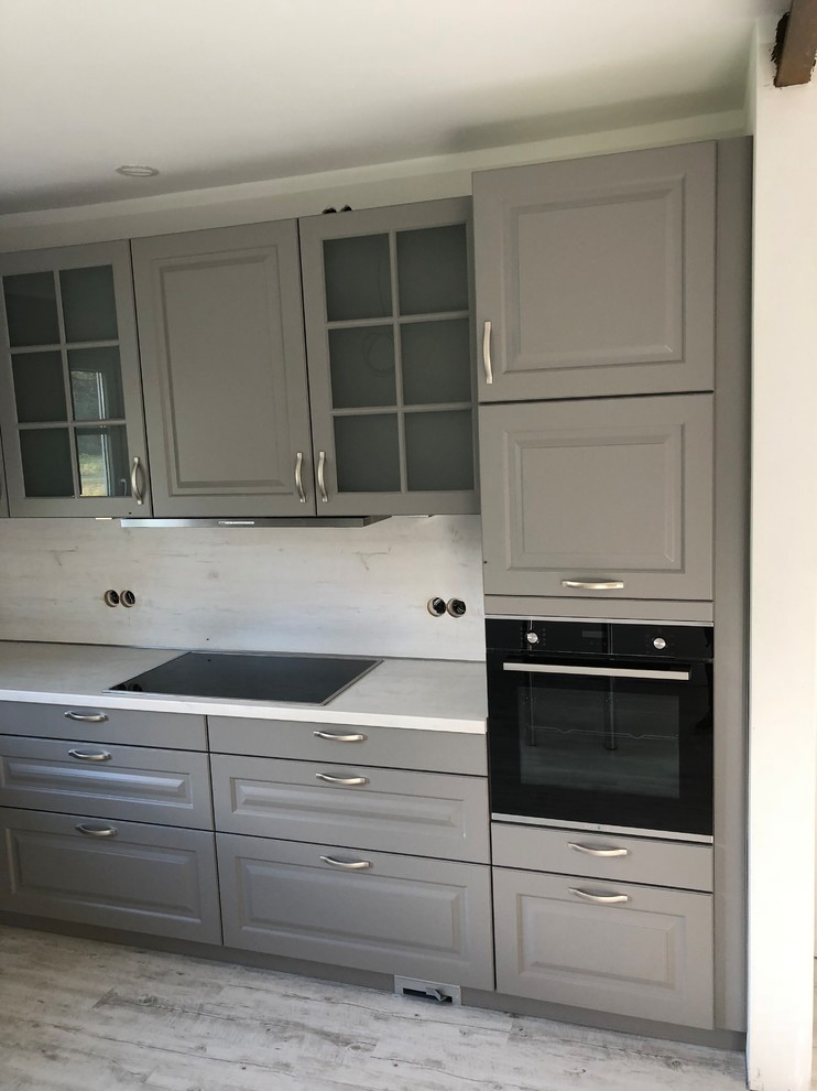 Large contemporary l-shaped open plan kitchen in Other with a built-in sink, beaded cabinets, grey cabinets, laminate countertops, white splashback, wood splashback, black appliances, light hardwood flooring, no island, grey floors and white worktops.