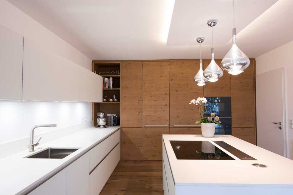 Moderne Küche in L-Form mit Unterbauwaschbecken, flächenbündigen Schrankfronten, weißen Schränken, Küchenrückwand in Weiß, schwarzen Elektrogeräten und Kücheninsel in Sonstige