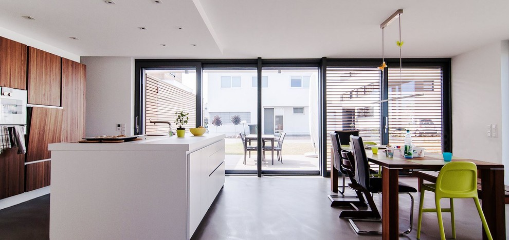 This is an example of a large modern kitchen/diner in Frankfurt with white cabinets, an island, a single-bowl sink, flat-panel cabinets and concrete flooring.