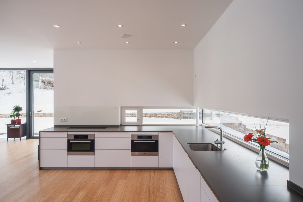 Design ideas for a modern l-shaped open plan kitchen in Other with a submerged sink, flat-panel cabinets, white cabinets, medium hardwood flooring, white splashback, integrated appliances and no island.