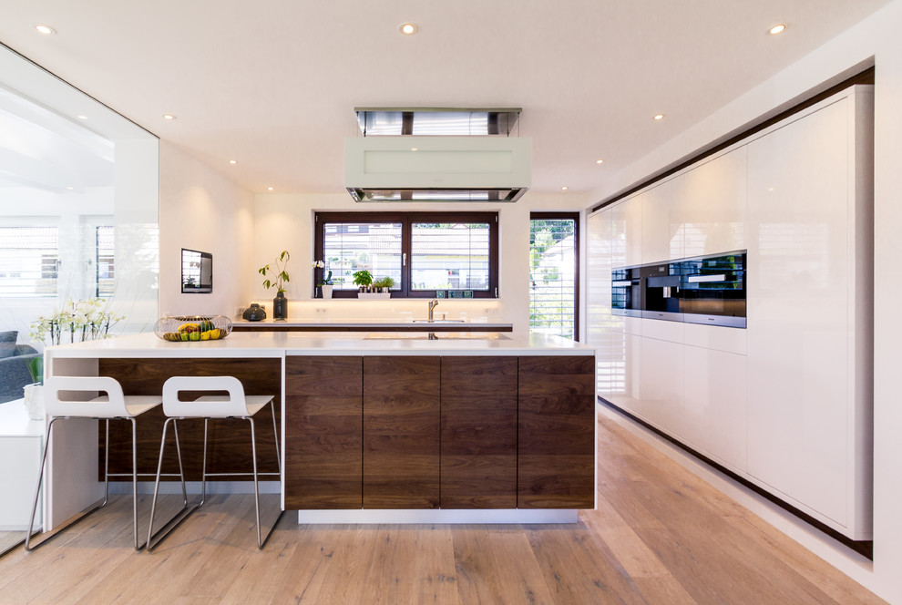 Inspiration for a mid-sized contemporary l-shaped medium tone wood floor and brown floor open concept kitchen remodel in Stuttgart with a drop-in sink, flat-panel cabinets, white cabinets, white backsplash, black appliances and a peninsula