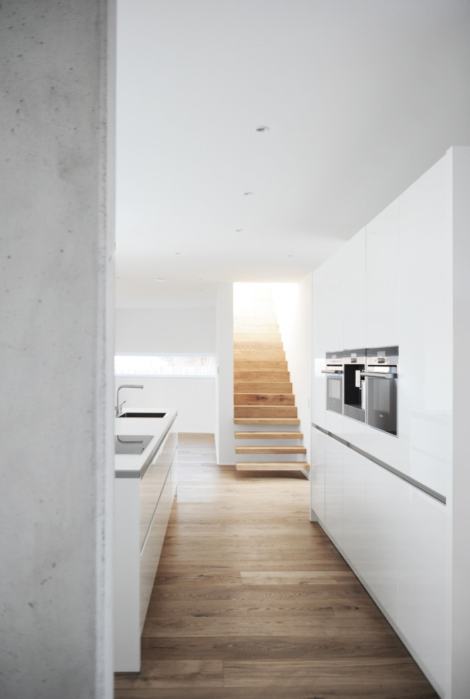 Photo of a medium sized contemporary galley kitchen in Bremen with a submerged sink, flat-panel cabinets, white cabinets, integrated appliances, an island, beige floors and white worktops.