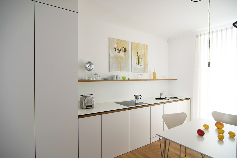 ミュンヘンにある小さなコンテンポラリースタイルのおしゃれなキッチン (ダブルシンク、フラットパネル扉のキャビネット、白いキャビネット、無垢フローリング、アイランドなし、白いキッチンパネル) の写真