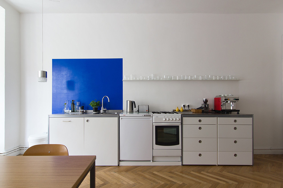 Inspiration for a large contemporary single-wall open plan kitchen in Berlin with a built-in sink, flat-panel cabinets, white cabinets, stainless steel worktops, blue splashback, limestone splashback, white appliances, dark hardwood flooring, no island and brown floors.