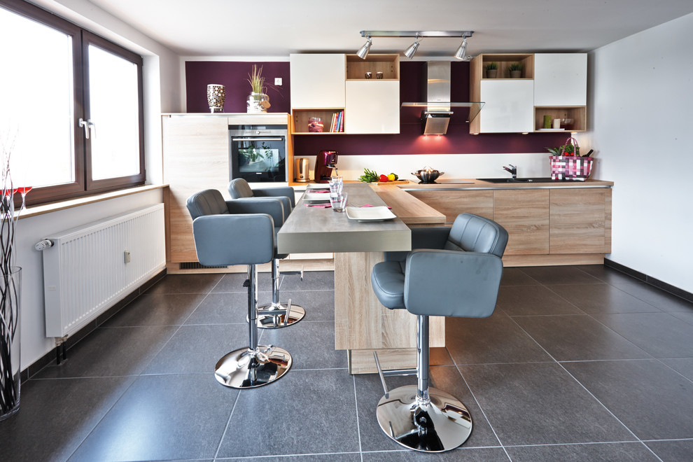 Example of a huge trendy single-wall gray floor eat-in kitchen design in Nuremberg with a drop-in sink, flat-panel cabinets, light wood cabinets, wood countertops, multicolored backsplash, black appliances and a peninsula