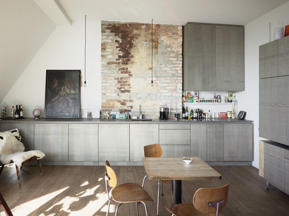 Foto på ett stort industriellt linjärt kök och matrum, med släta luckor, mellanmörkt trägolv, grå skåp, en integrerad diskho och flerfärgad stänkskydd