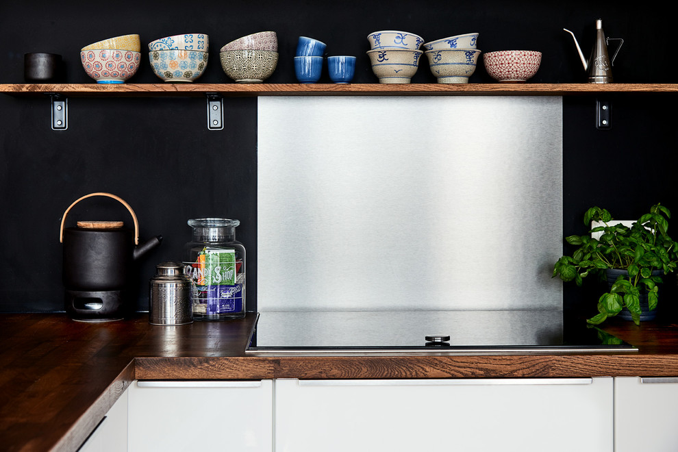 Landhausstil Küche mit flächenbündigen Schrankfronten, weißen Schränken, Arbeitsplatte aus Holz, Küchenrückwand in Schwarz und schwarzen Elektrogeräten in Berlin