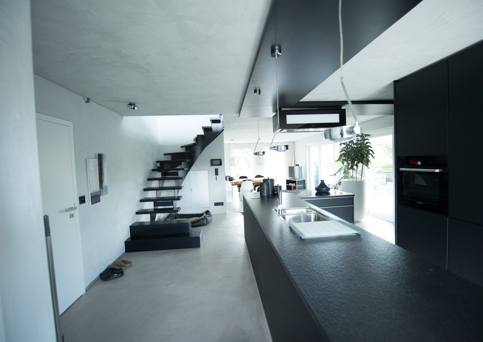Idéer för mellanstora funkis svart kök, med en dubbel diskho, släta luckor, svarta skåp, granitbänkskiva, betonggolv, en köksö, svart stänkskydd, rostfria vitvaror och grått golv