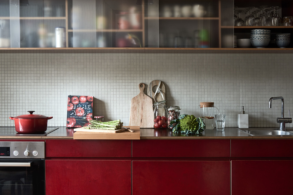 Bild på ett funkis kök, med en nedsänkt diskho, röda skåp, träbänkskiva, vitt stänkskydd och stänkskydd i mosaik