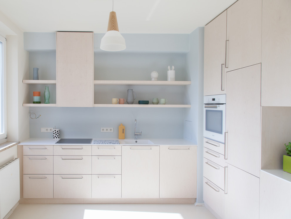 Cette image montre une petite cuisine ouverte nordique en L et bois clair avec un évier intégré, un placard à porte plane, une crédence bleue, un électroménager blanc, aucun îlot, un sol beige et un plan de travail blanc.