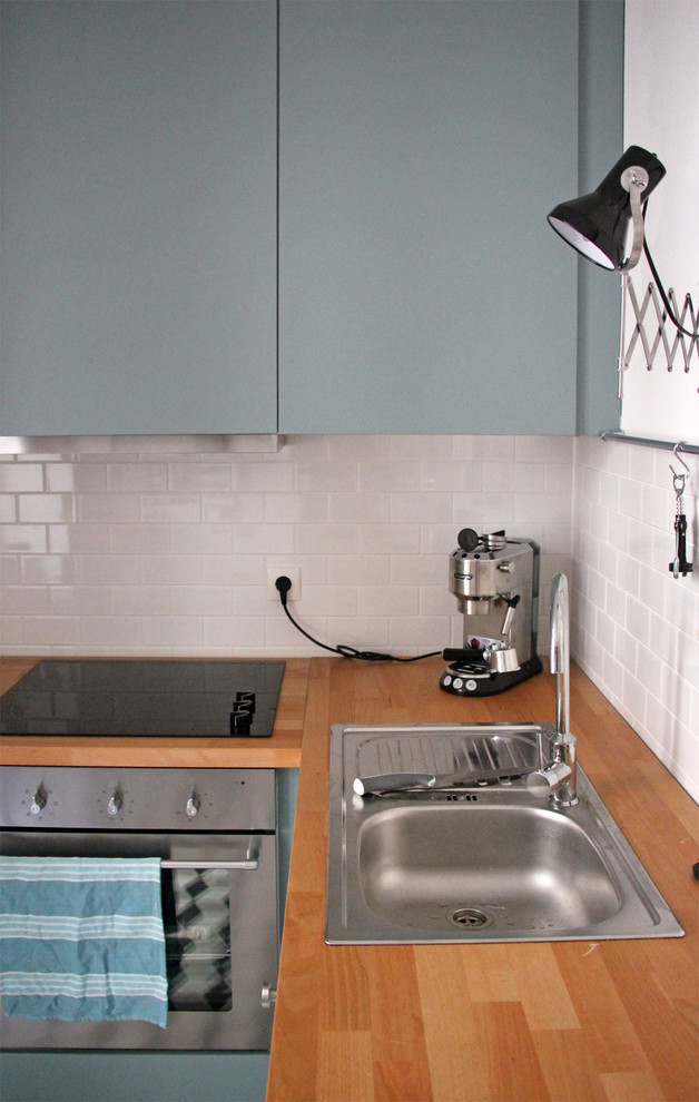 Stilmix Wohnküche in L-Form mit Einbauwaschbecken, blauen Schränken, Arbeitsplatte aus Holz, Küchenrückwand in Weiß und Küchengeräten aus Edelstahl in Berlin