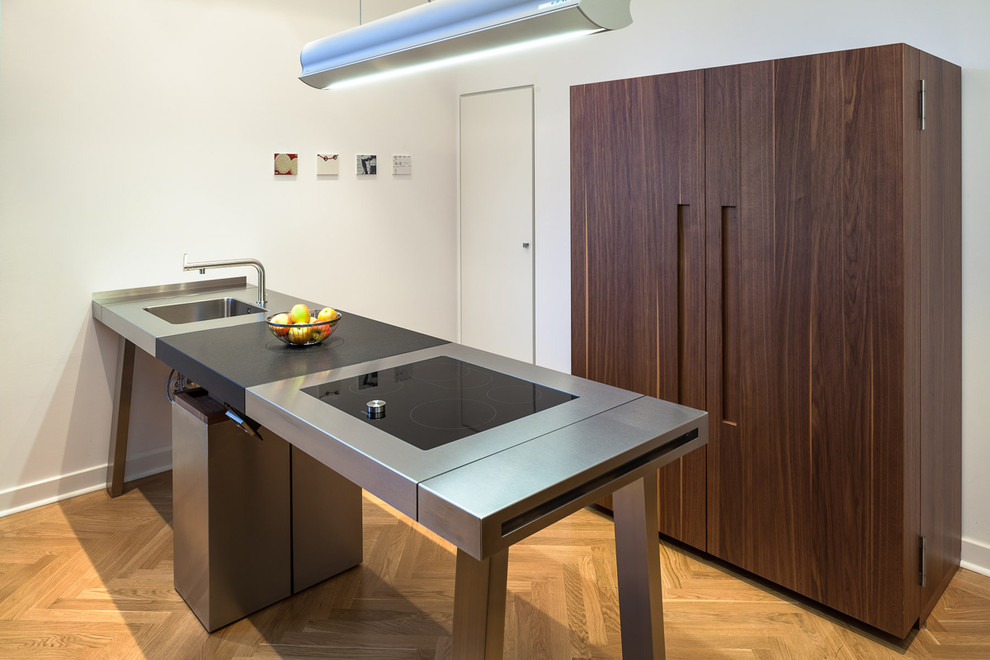 This is an example of a medium sized contemporary kitchen in Dusseldorf with an integrated sink, flat-panel cabinets, dark wood cabinets, stainless steel worktops, medium hardwood flooring and a breakfast bar.