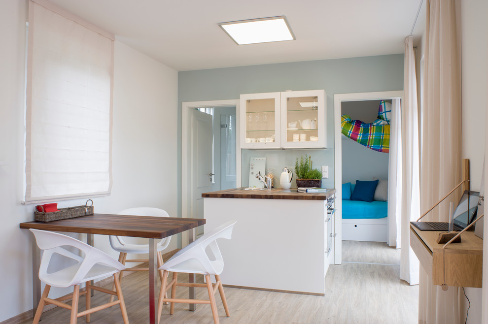 Photo of a small contemporary single-wall enclosed kitchen in Other with a built-in sink, glass-front cabinets, white cabinets, wood worktops, blue splashback, glass sheet splashback, stainless steel appliances, medium hardwood flooring and no island.
