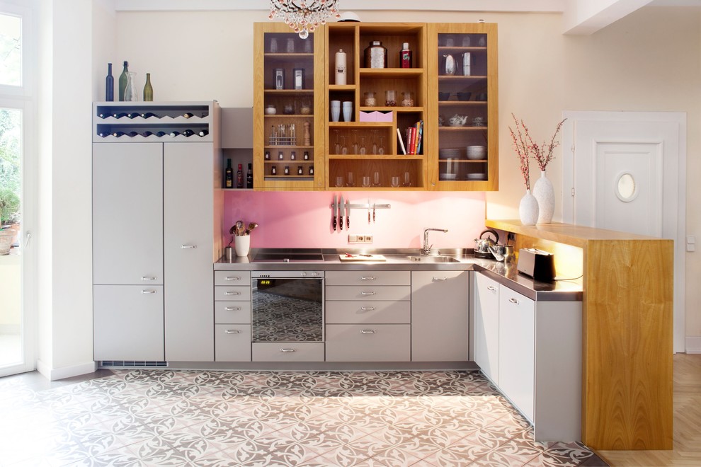 Inredning av ett modernt mycket stort grå grått kök, med en integrerad diskho, släta luckor, grå skåp, bänkskiva i rostfritt stål, rosa stänkskydd, stänkskydd i trä, cementgolv och flerfärgat golv