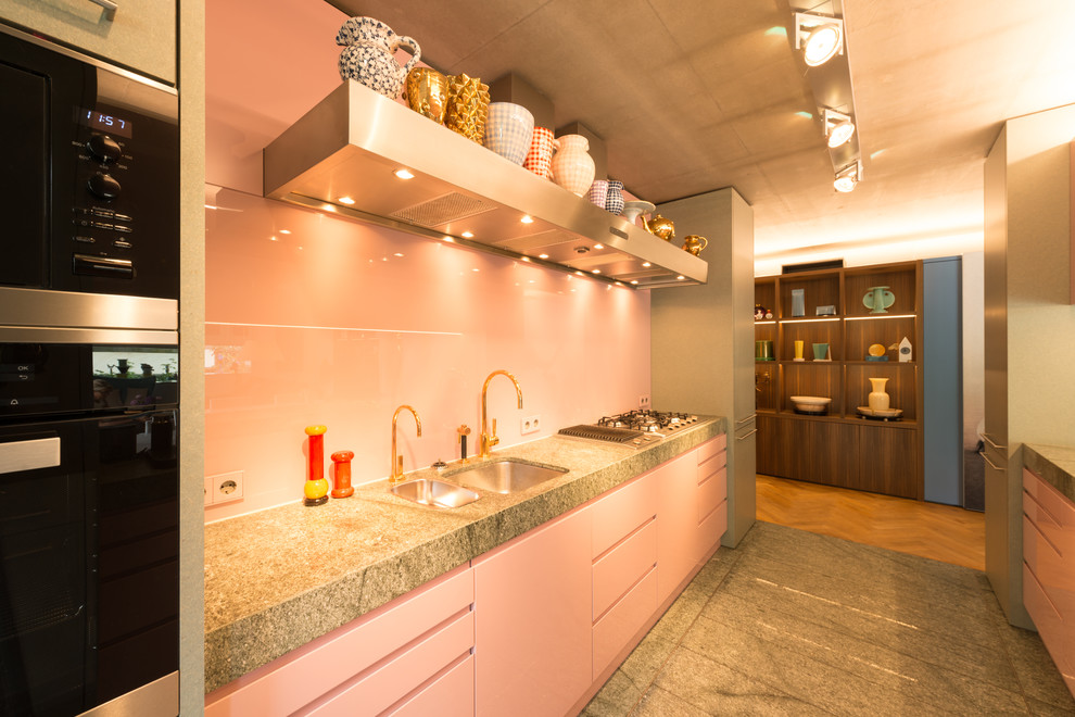 Offene, Zweizeilige, Mittelgroße Mid-Century Küche mit Waschbecken, flächenbündigen Schrankfronten, Granit-Arbeitsplatte, Küchenrückwand in Rosa, Glasrückwand, Kücheninsel und grauem Boden in Sonstige