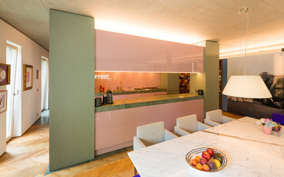 Идея дизайна: параллельная кухня-гостиная среднего размера в стиле ретро с одинарной мойкой, плоскими фасадами, гранитной столешницей, розовым фартуком, фартуком из стекла, островом и серым полом