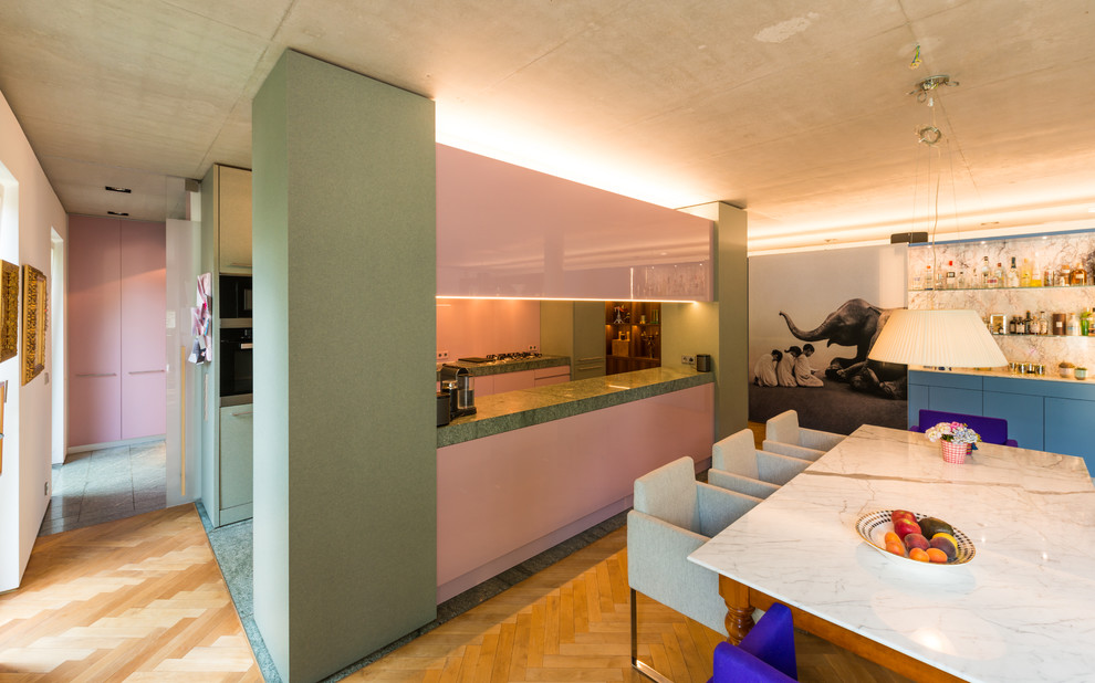 Свежая идея для дизайна: параллельная кухня-гостиная среднего размера в стиле ретро с одинарной мойкой, плоскими фасадами, гранитной столешницей, розовым фартуком, фартуком из стекла, островом и серым полом - отличное фото интерьера