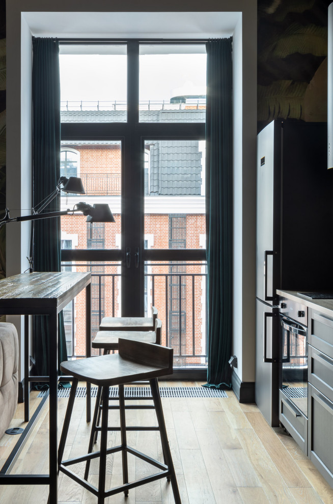 Small urban single-wall open plan kitchen in Moscow with a built-in sink, raised-panel cabinets, black cabinets, laminate countertops, black appliances, light hardwood flooring, an island, beige floors and beige worktops.