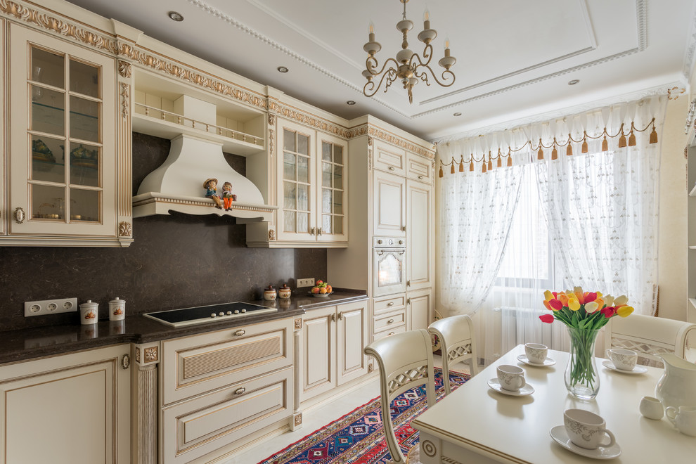 Exemple d'une cuisine américaine linéaire chic avec des portes de placard beiges, une crédence noire et un placard avec porte à panneau surélevé.