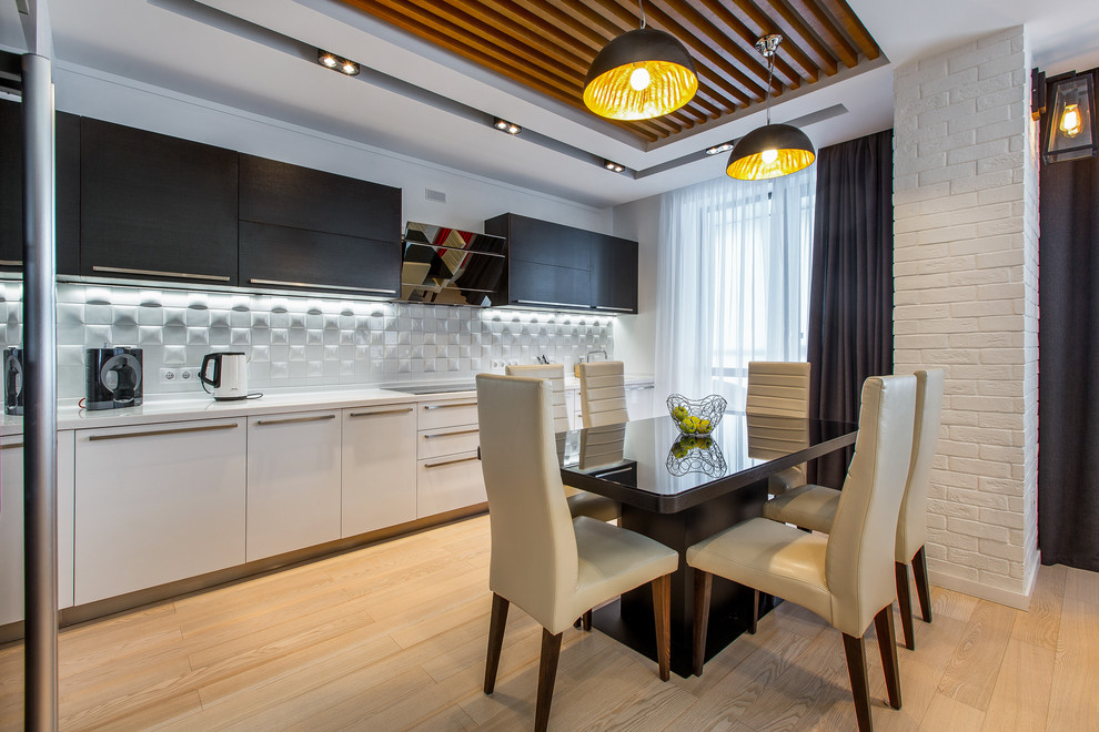 Einzeilige Moderne Wohnküche ohne Insel mit flächenbündigen Schrankfronten, weißen Schränken, Küchenrückwand in Weiß und hellem Holzboden in Sonstige