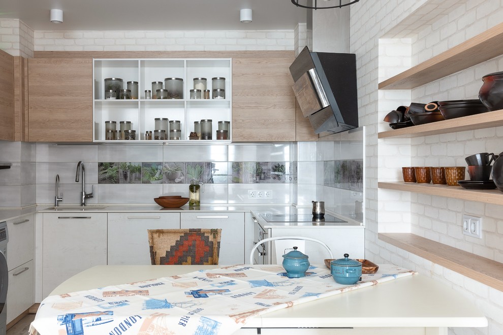 На фото: п-образная, светлая кухня в современном стиле с врезной мойкой, плоскими фасадами, белыми фасадами, разноцветным фартуком и белой столешницей