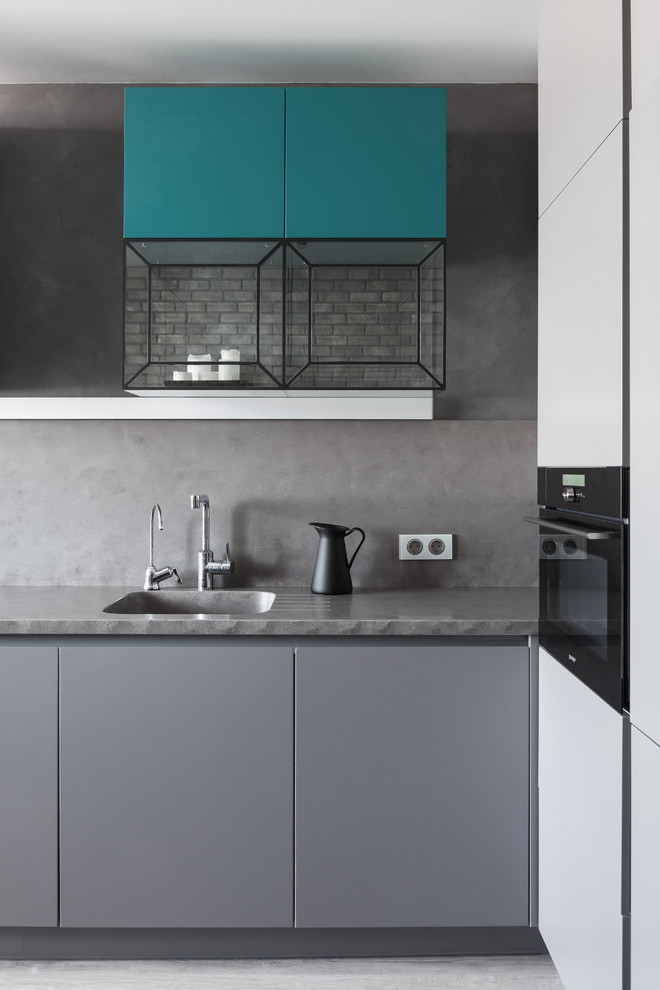 Imagen de cocina contemporánea de tamaño medio con fregadero bajoencimera, armarios con paneles lisos, puertas de armario grises, salpicadero verde, electrodomésticos negros, suelo laminado y suelo gris