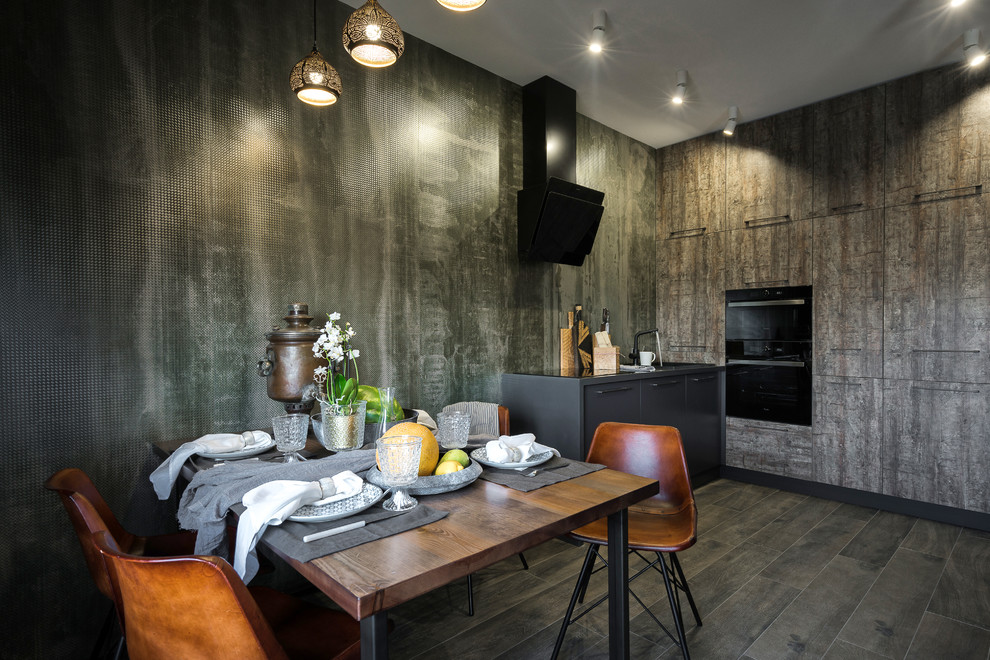 Ejemplo de cocina comedor actual con armarios con paneles lisos, puertas de armario con efecto envejecido, electrodomésticos negros y suelo marrón