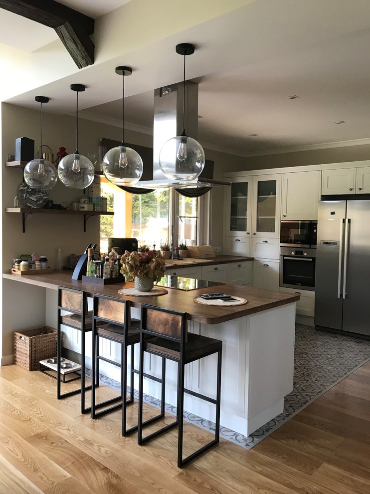 Idéer för att renovera ett stort medelhavsstil brun brunt kök, med luckor med upphöjd panel, vita skåp, träbänkskiva, rostfria vitvaror och en halv köksö